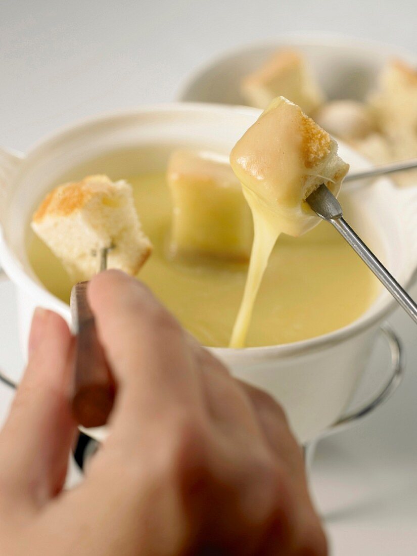 Cheese fondue with cubes of bread and hand