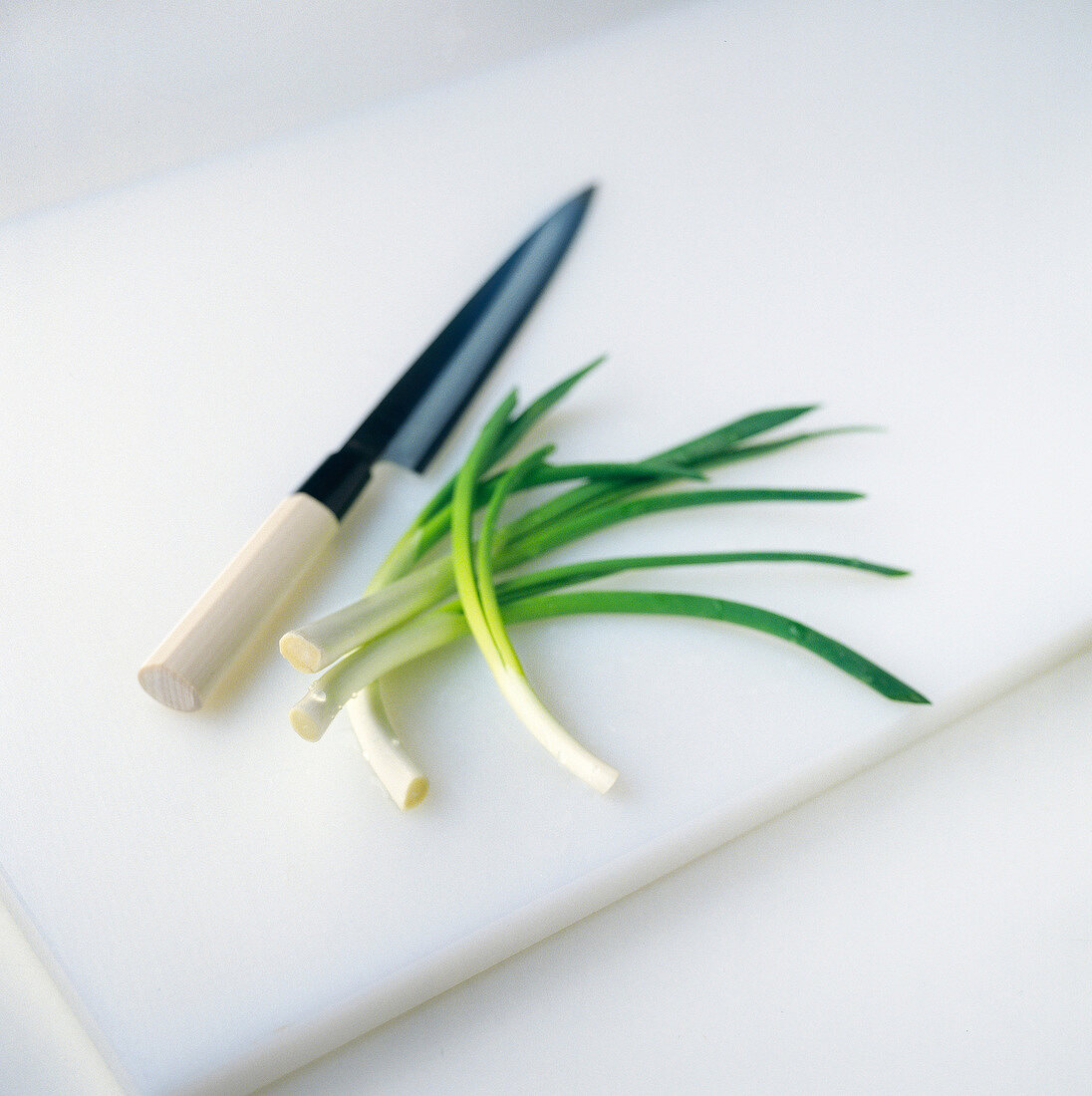 Frühlingszwiebeln auf Küchenbrett mit Messer