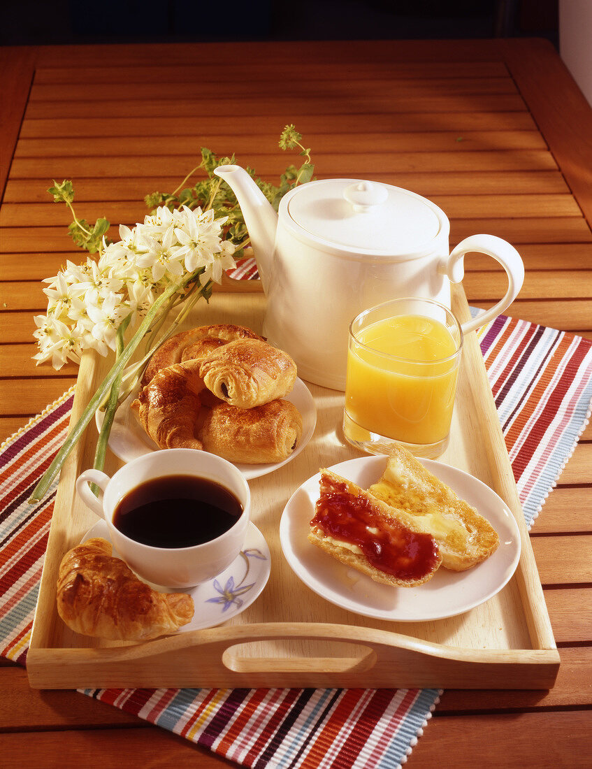 Frühstück auf einem Tablett, mit Kaffee, Marmeladenbrot, Orangensaft, Croissant und Schokobrötchen