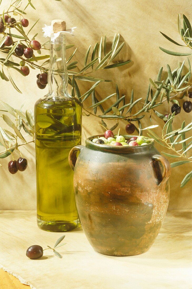 Eine Flasche Olivenöl mit frischen Oliven im Krug