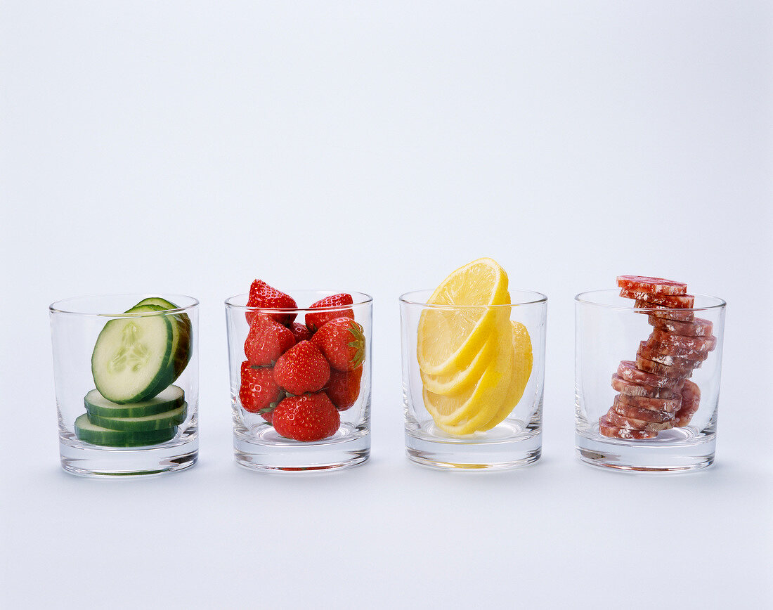 Gurkenscheiben, Erdbeeren, Zitronenscheiben und Salami in vier Gläsern
