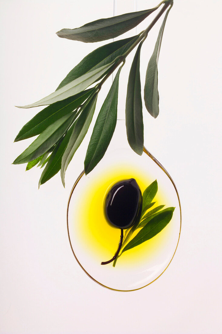 Eine Olive mit Olivenöl auf durchsichtigem Löffel