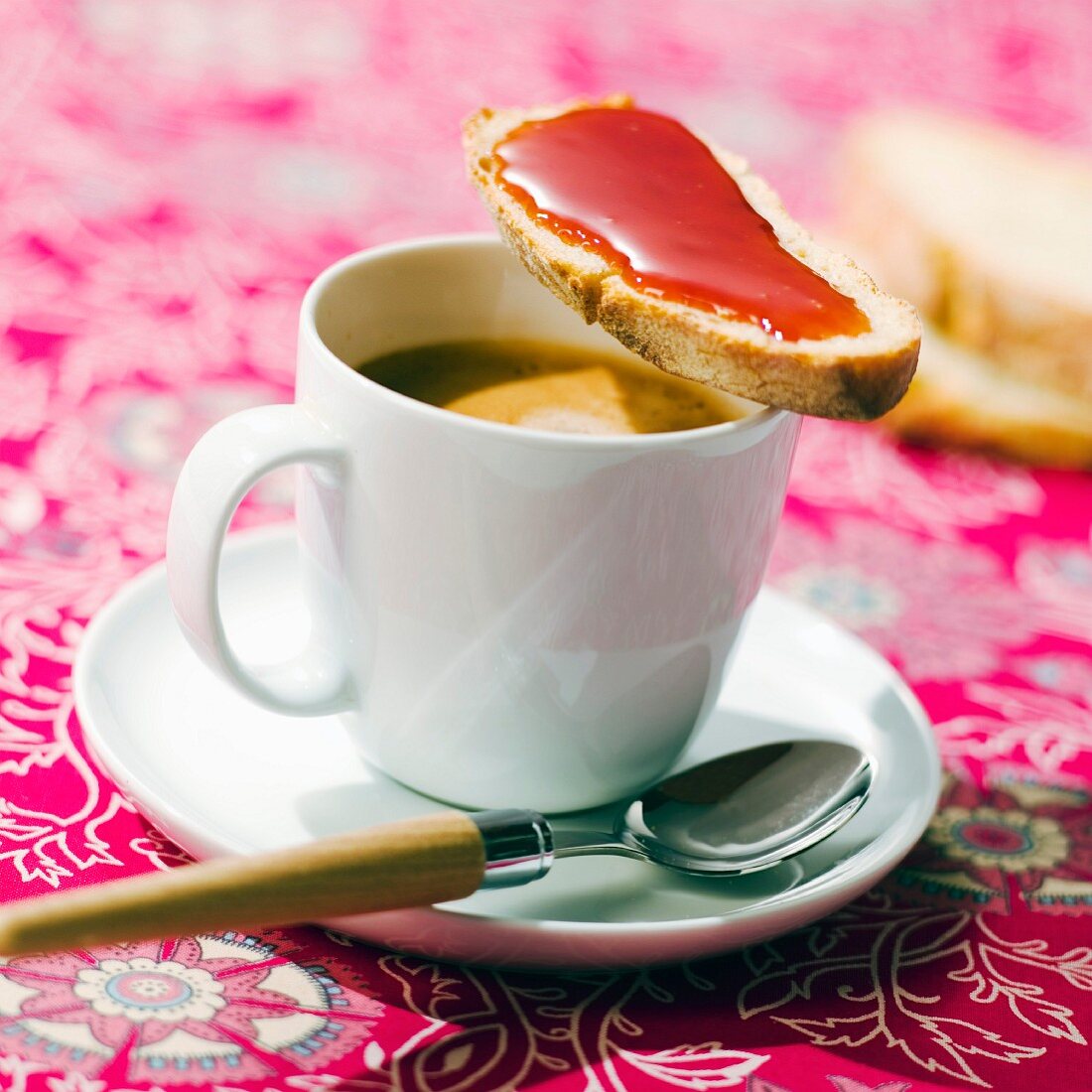 Weißbrot mit Hagebuttenmarmelade auf Kaffeetasse mit Milchkaffee