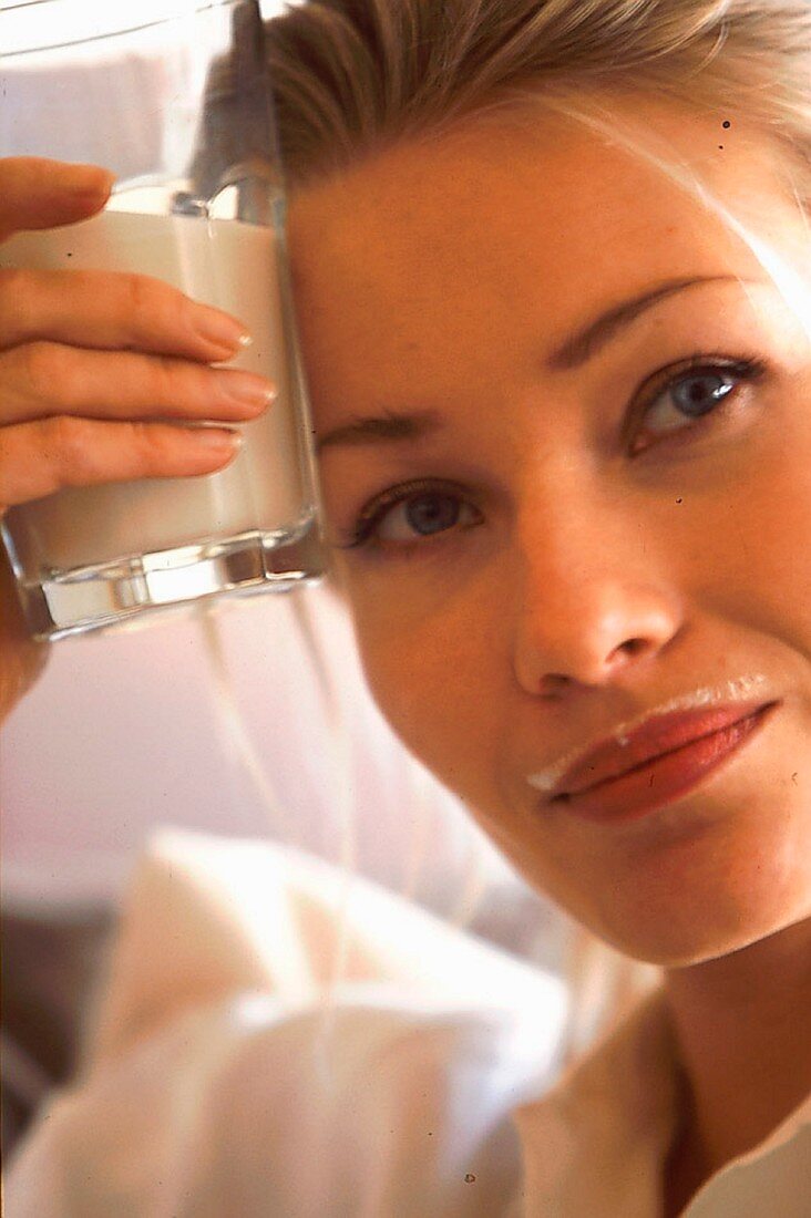 Frau hält ein Glas Milch an die Stirn