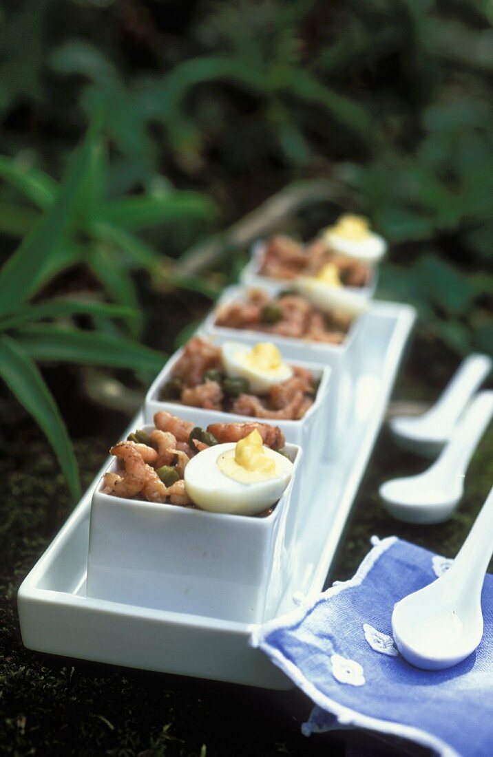 Shrimp salad with capers and quail's eggs in square bowls