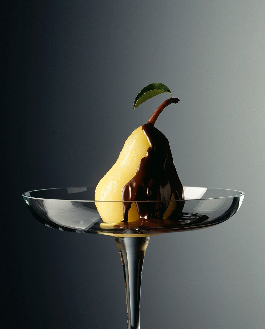 A pear with dark chocolate sauce on a glass plate