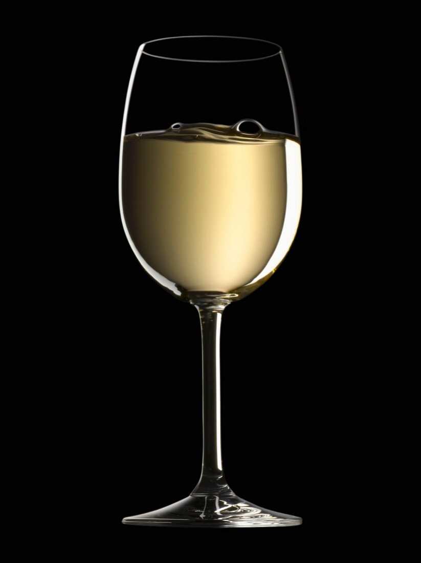 Ein Glas Weißwein vor schwarzem Hintergrund