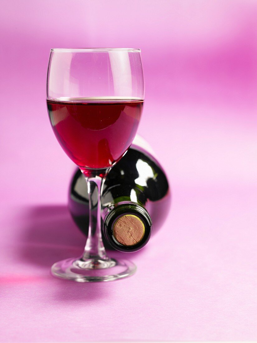 Glas mit Rotwein und Weinflasche dahinter