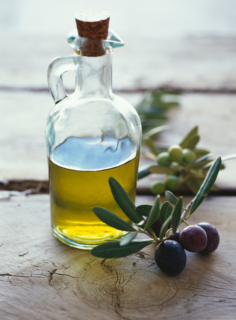 Flasche mit Olivenöl, daneben Olivenzweig