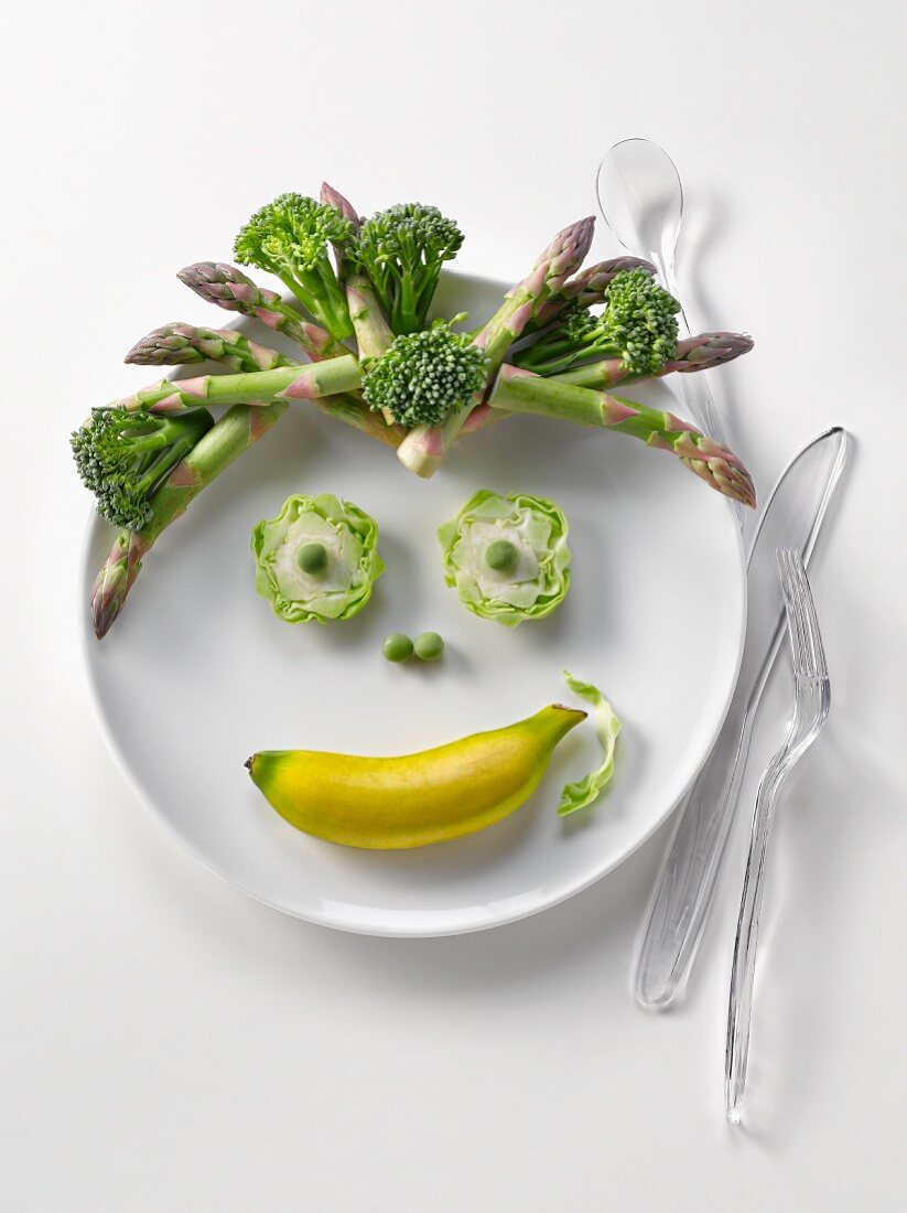 Plate of green vegetables and mini banana in the shape of a face