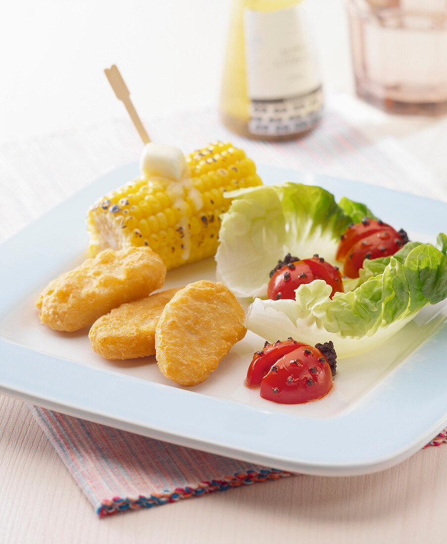 Homemade chicken nuggets with ladybug tomatoes and sweet corn on the cob