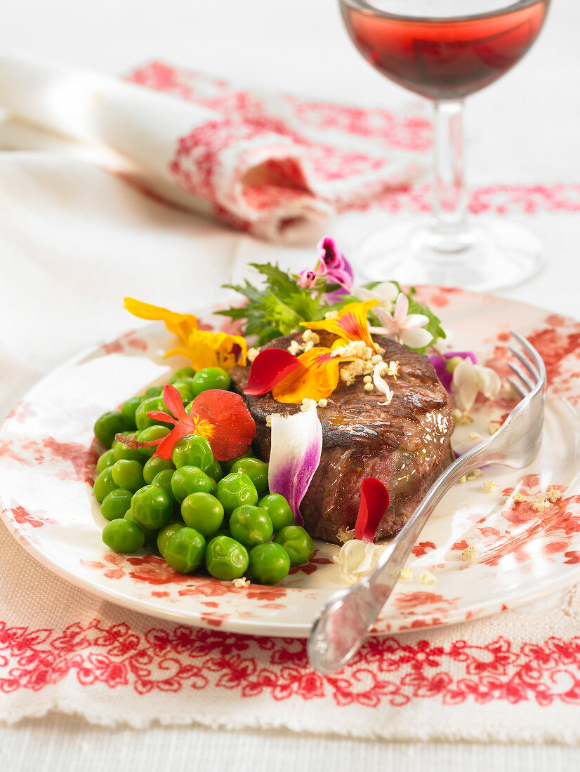 Veal steak with edible flowers and peas