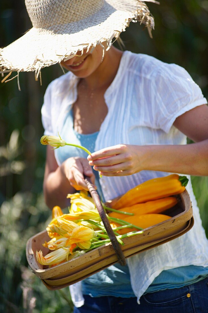 Frau mit Sonnenhut trägt einen Korb mit Zucchiniblüten
