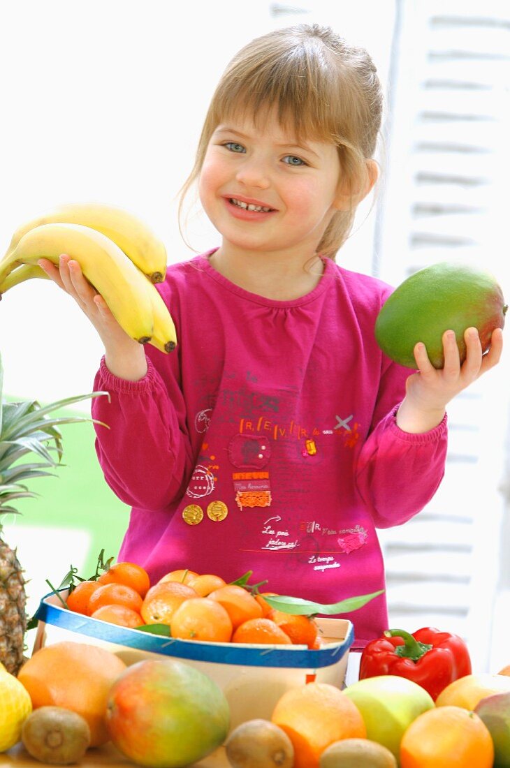 Kleines Mädchen hält Bananen und Mango