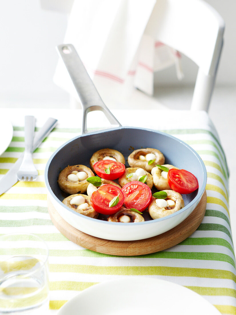 Gebratene Pilze in der Pfanne mit Knoblauch, Mozzarella, Tomaten und Basilikum