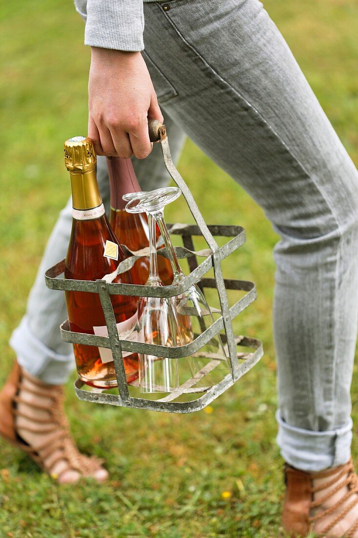 Person holding a metal bottle carrier with glasses and bottles of Champagne