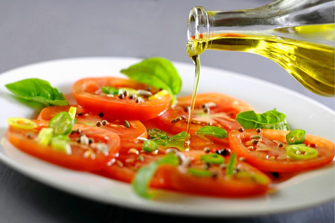 Olivenöl über Tomaten-Basilikum-Salat träufeln