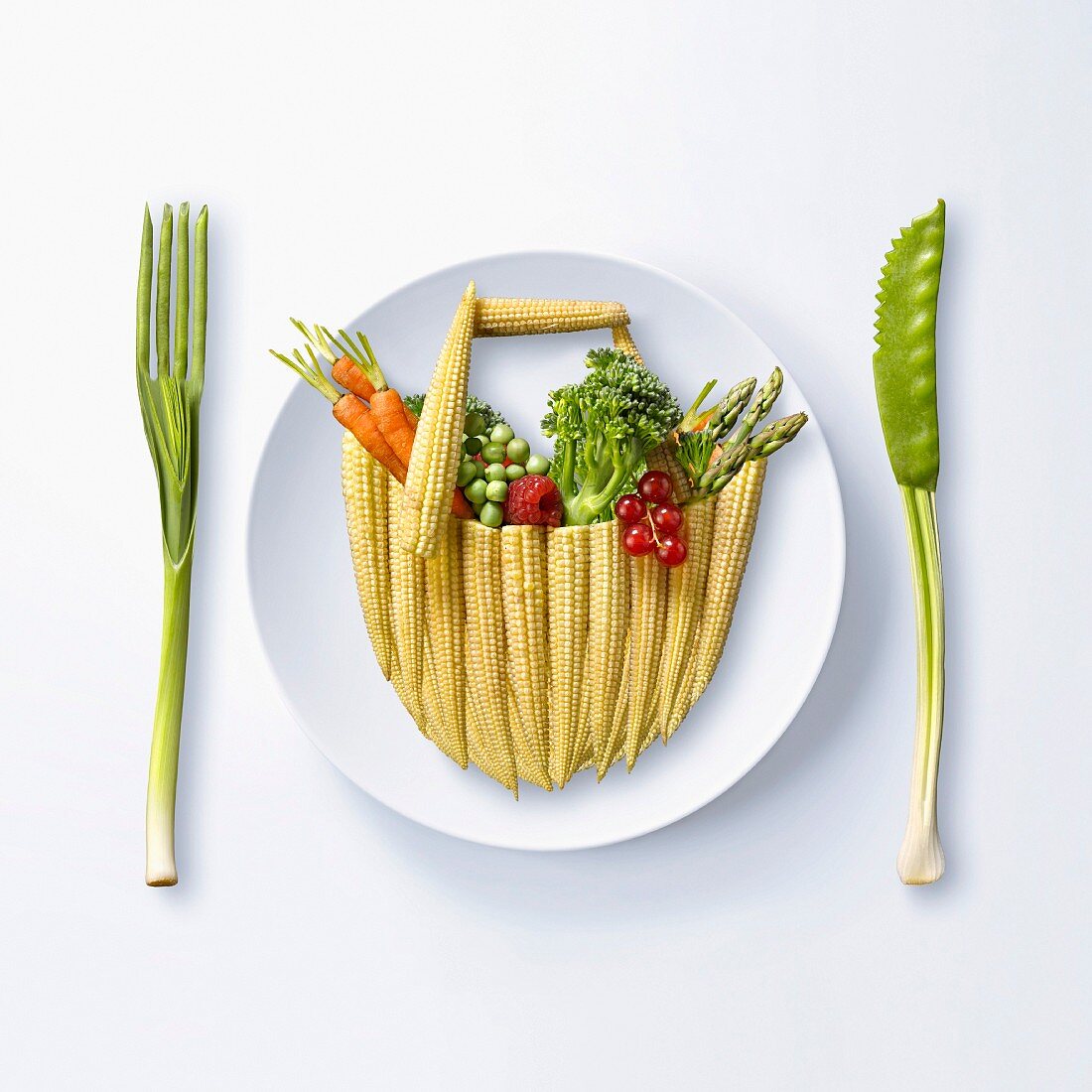 Obst und Gemüse in Form eines Einkaufskorbs auf Teller, daneben Besteck aus Gemüse (Symbolbild)