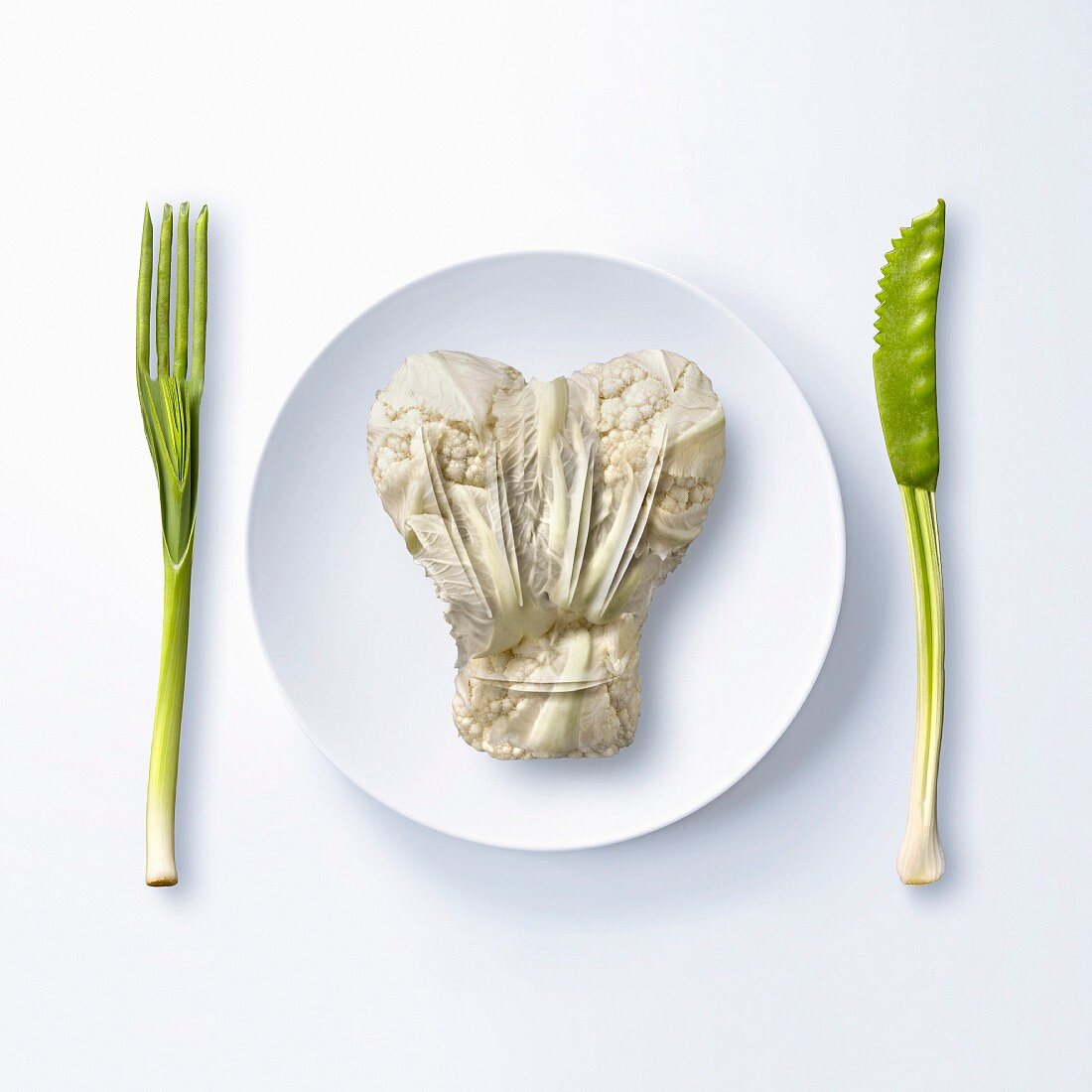 Blumenkohl in Form einer Kochhaube auf Teller, daneben Besteck aus Gemüse (Symbolbild)