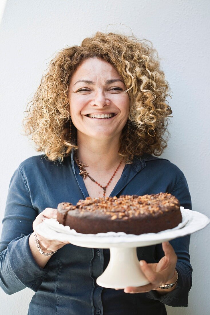 Frau hält einen Tortenständer mit Schokoladekuchen