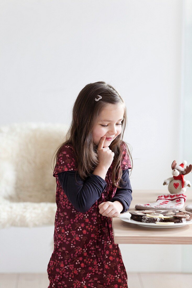 Young girl hesitating infront of a plate of chocolate biscuits