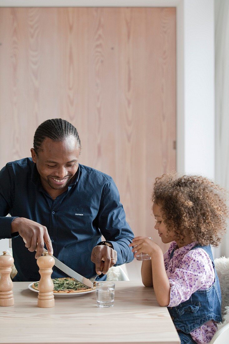 Man cutting a slice of pizza for his daughter