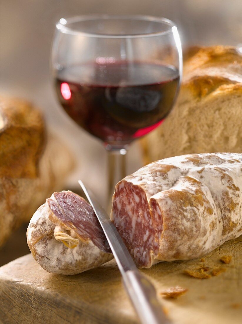 Angeschnittene Salami mit Brot und einem Glas Rotwein