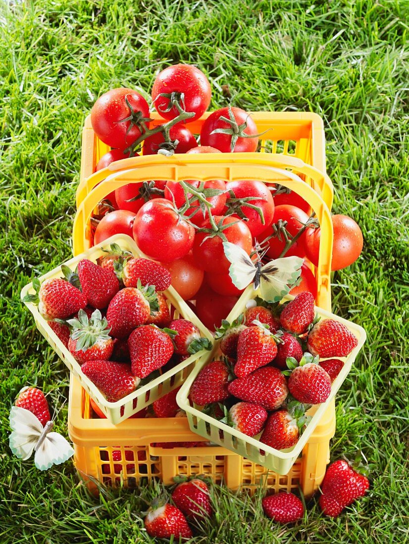 Steige mit Tomaten und zwei Körbchen mit Erdbeeren