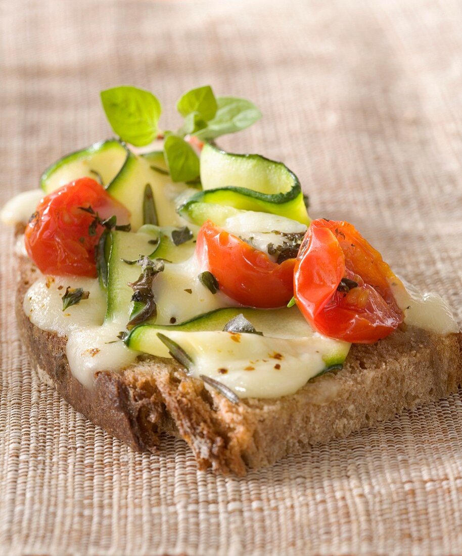 Belegtes Brot mit Morbier-Käse, Zucchini, Tomate und Kräutern