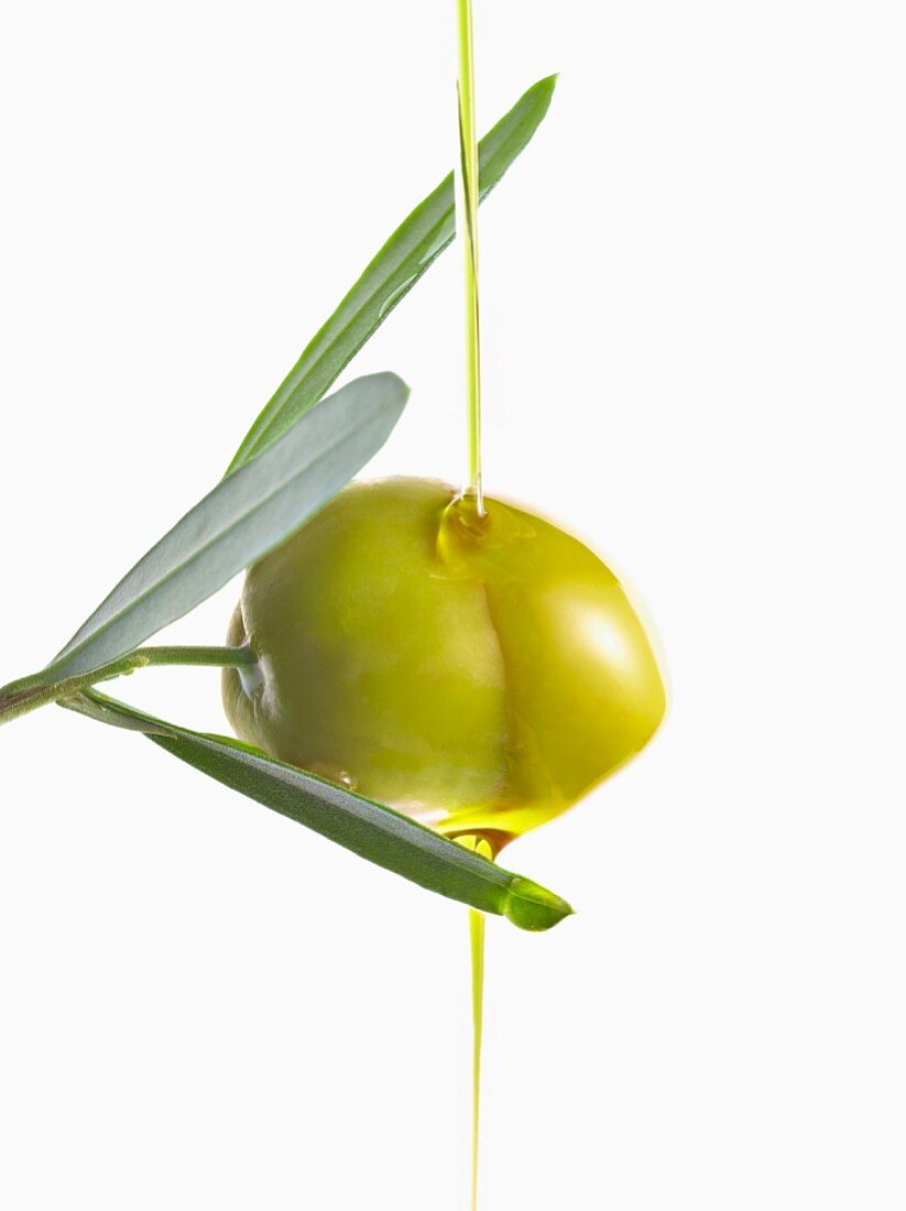 Olivenöl fliesst über eine grüne Olive