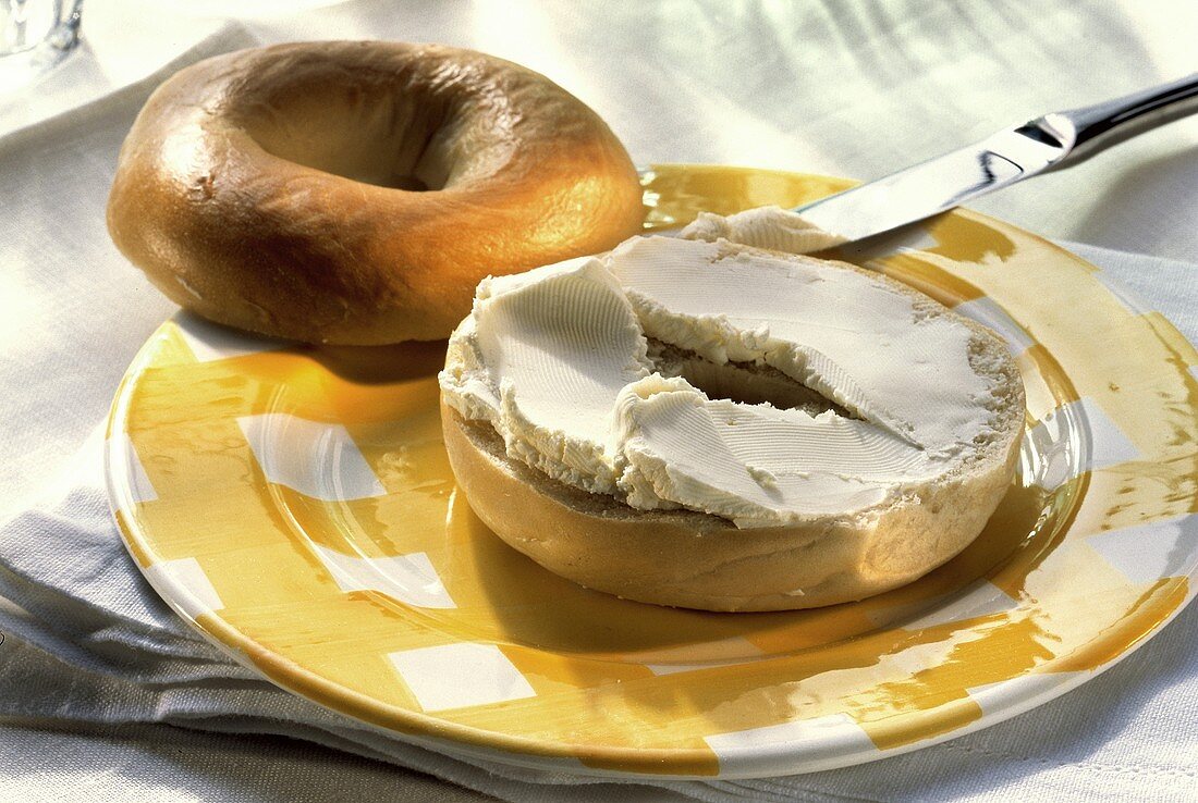 Ringförmiges Brötchen (Bagel) mit Rahmfrischkäse auf Teller