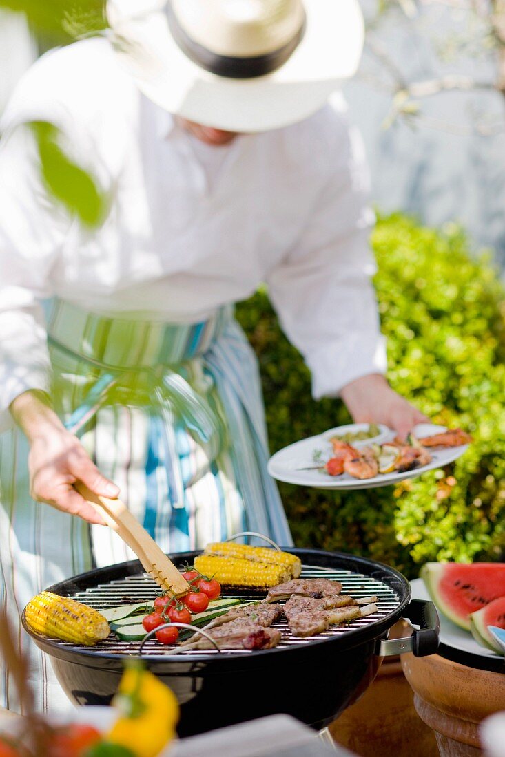 Person grillt Fleisch und Gemüse im Freien