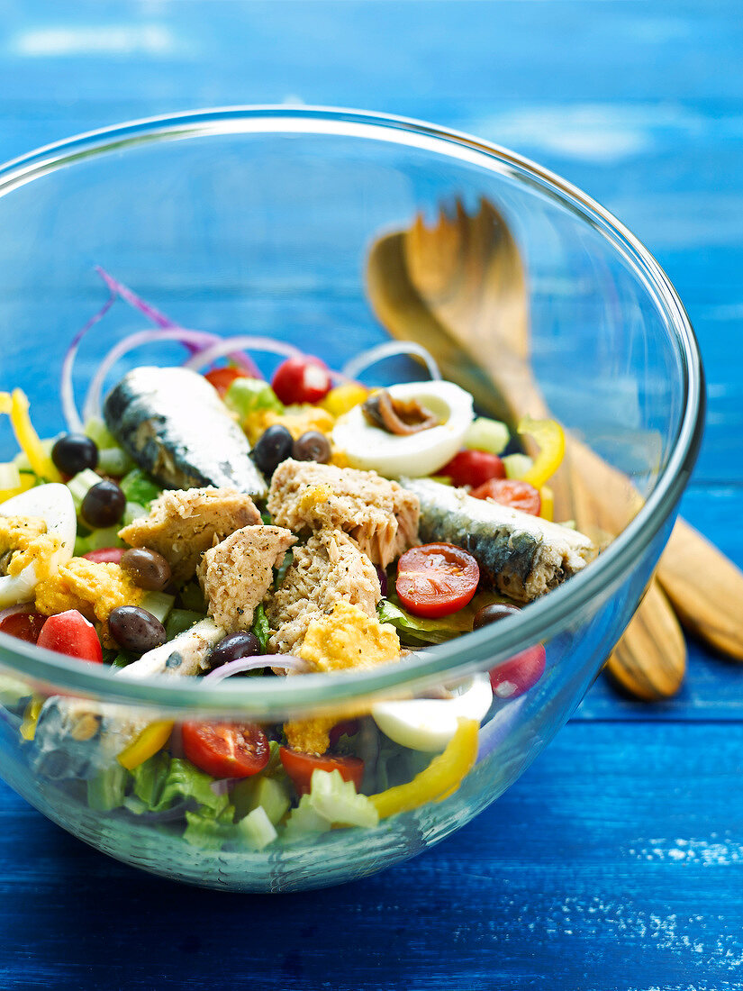 Gemischter Salat mit Sardinen, Thunfisch, Ei und Oliven in einer Salatschüssel mit Holzbesteck