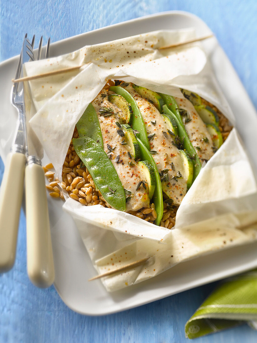 Sliced chicken breasts with zucchinis,sweet peas and spelt cooked in wax paper