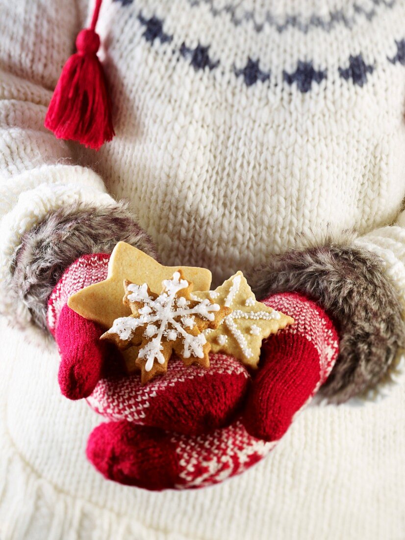 Person wearing muffles and holding star-shaped shortbread Christmas cookies