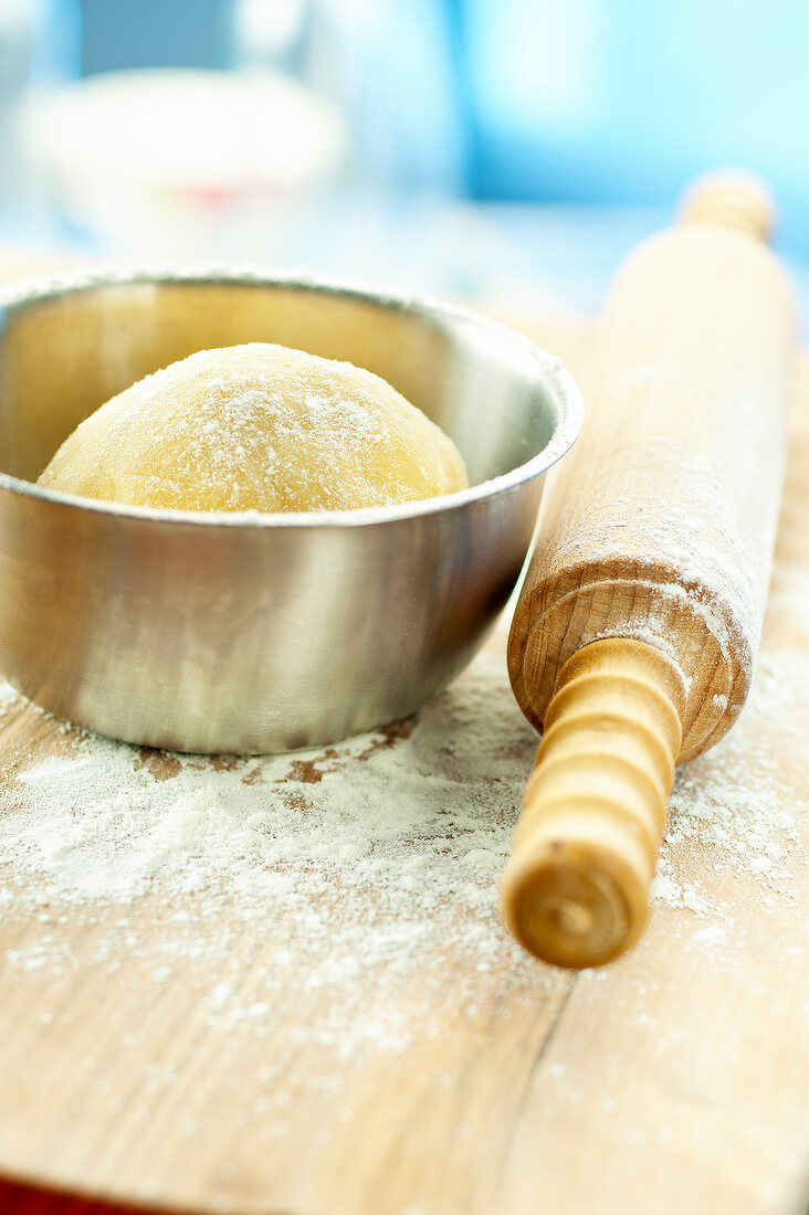 Teigkugel in einer Schüssel und Nudelholz auf bemehltem Holzbrett