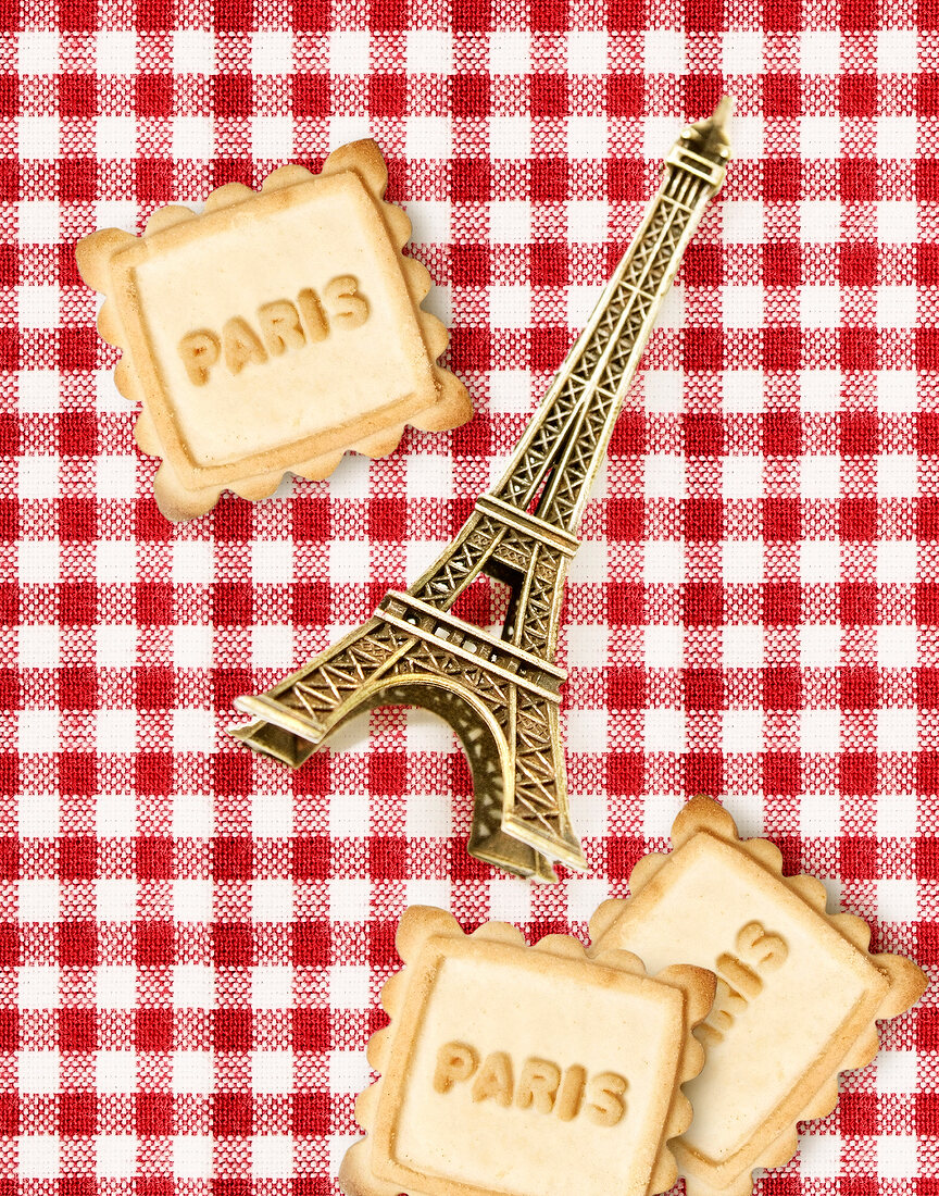 Komposition mit Mini-Eiffelturm und Plätzchen mit Aufschrift Paris auf rot-weiss-karierter Tischdecke
