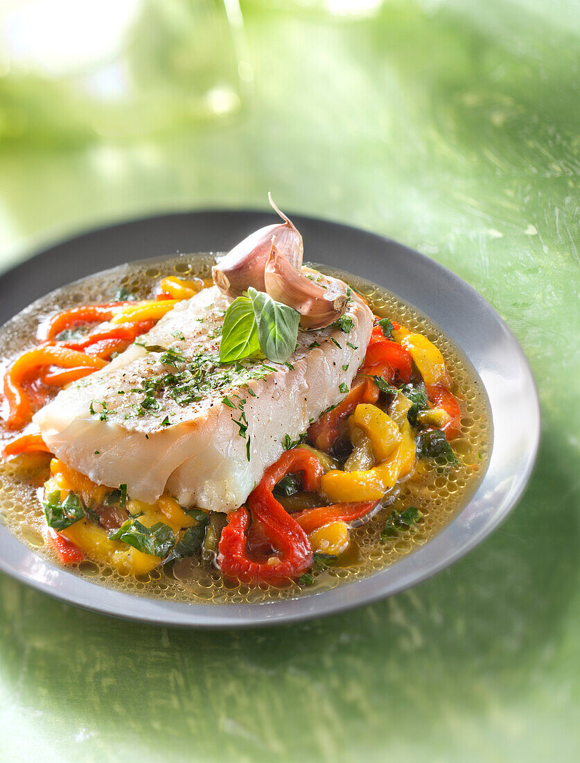 Piece of cod with pink garlic and tarragon on a bed of warm bell pepper salad