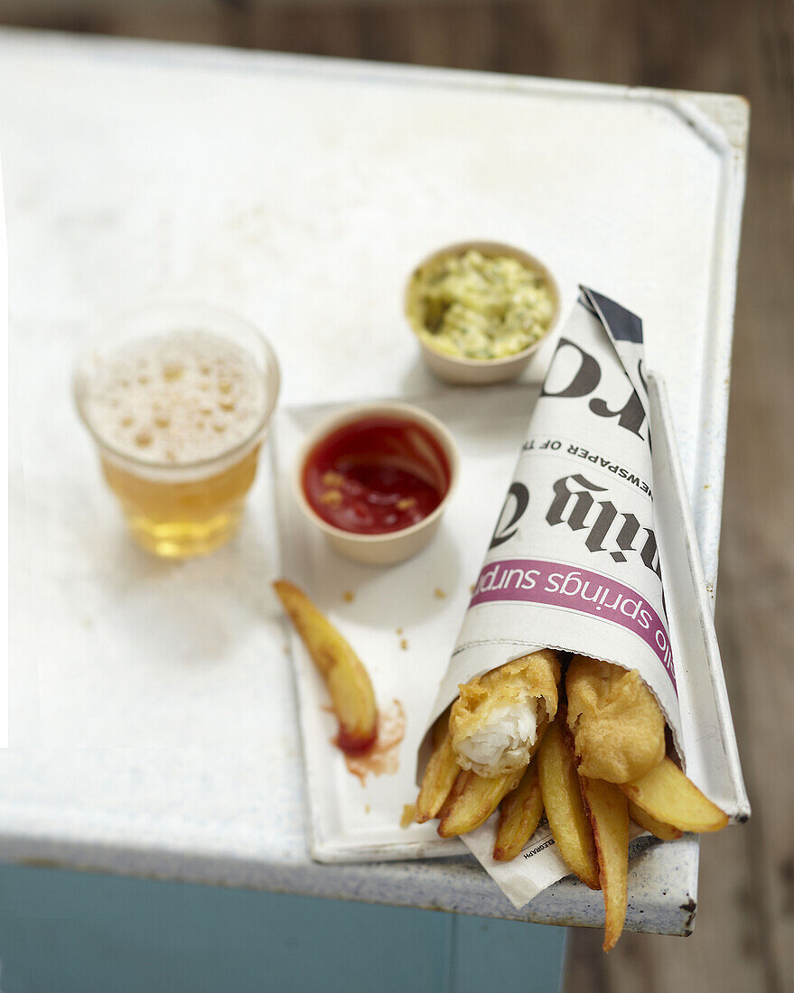 Fish and Chips in Zeitungspapier gewickelt mit Dips und einem Glas Bier
