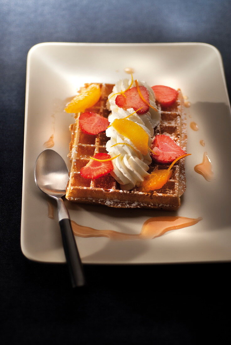 Waffle topped with sliced strawberries, orange and whipped cream