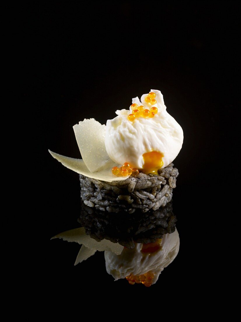 Schwarzes Risotto mit pochiertem Ei, Lachsrogen und Parmesanspänen auf schwarzem Hintergrund