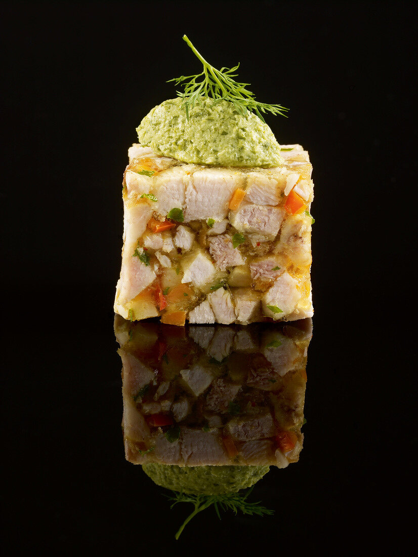 Rabbit and aspic terrine topped with a sorrel quenelle on a black background