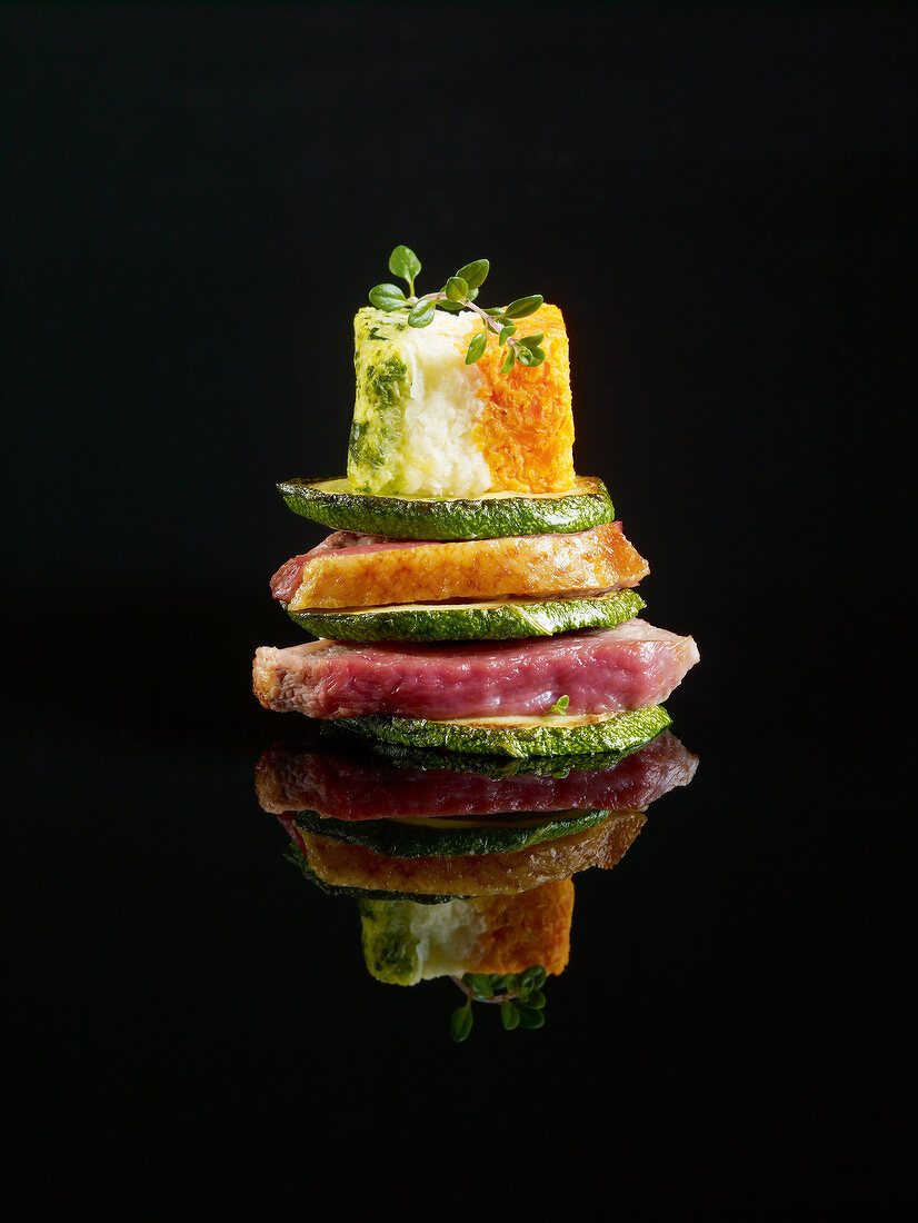 Layered duckling and zucchinis topped with a mini vegetable Bavarian on a black background