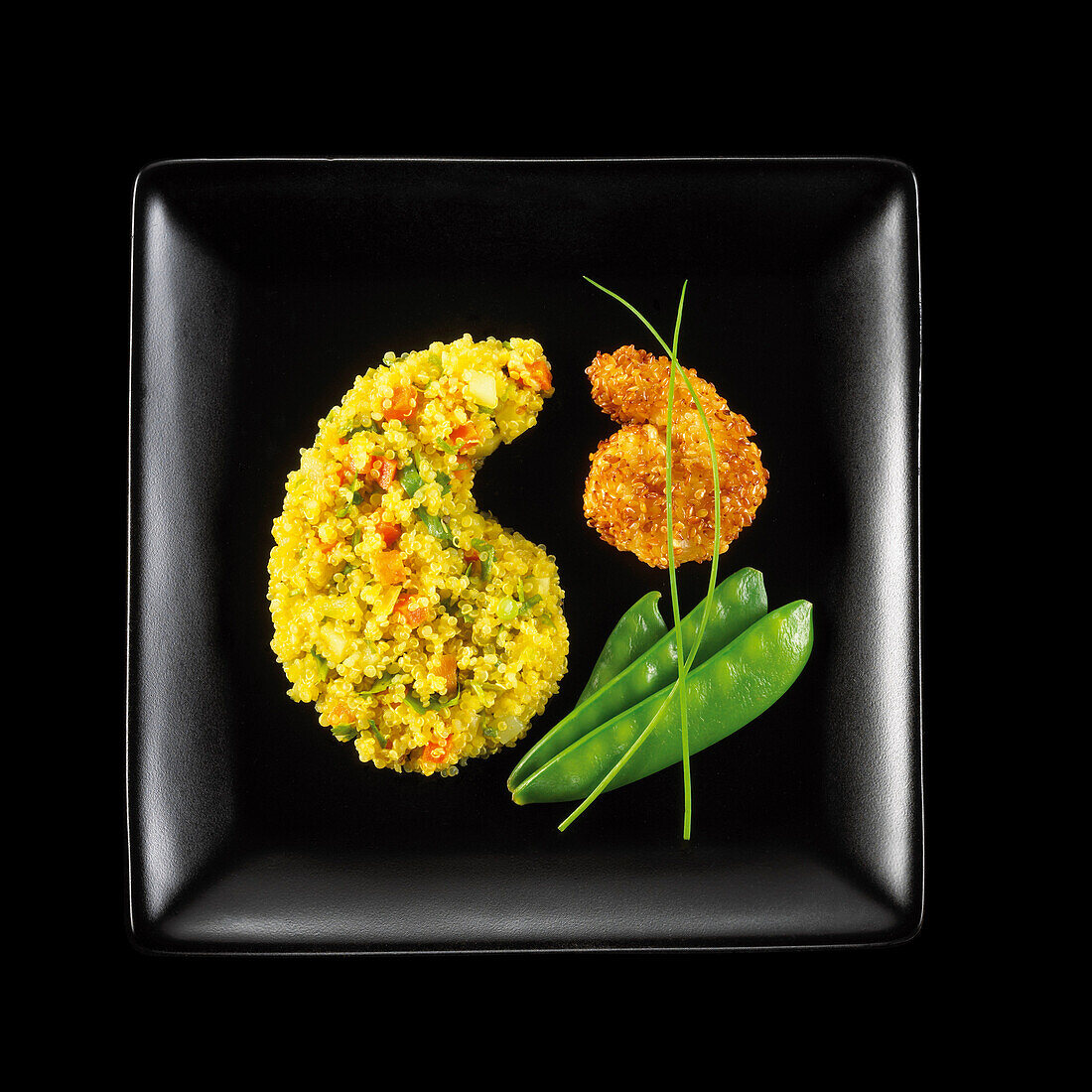 Fried king prawn coated in sesame seeds,yellow quinoa and crisp vegetables on a black background