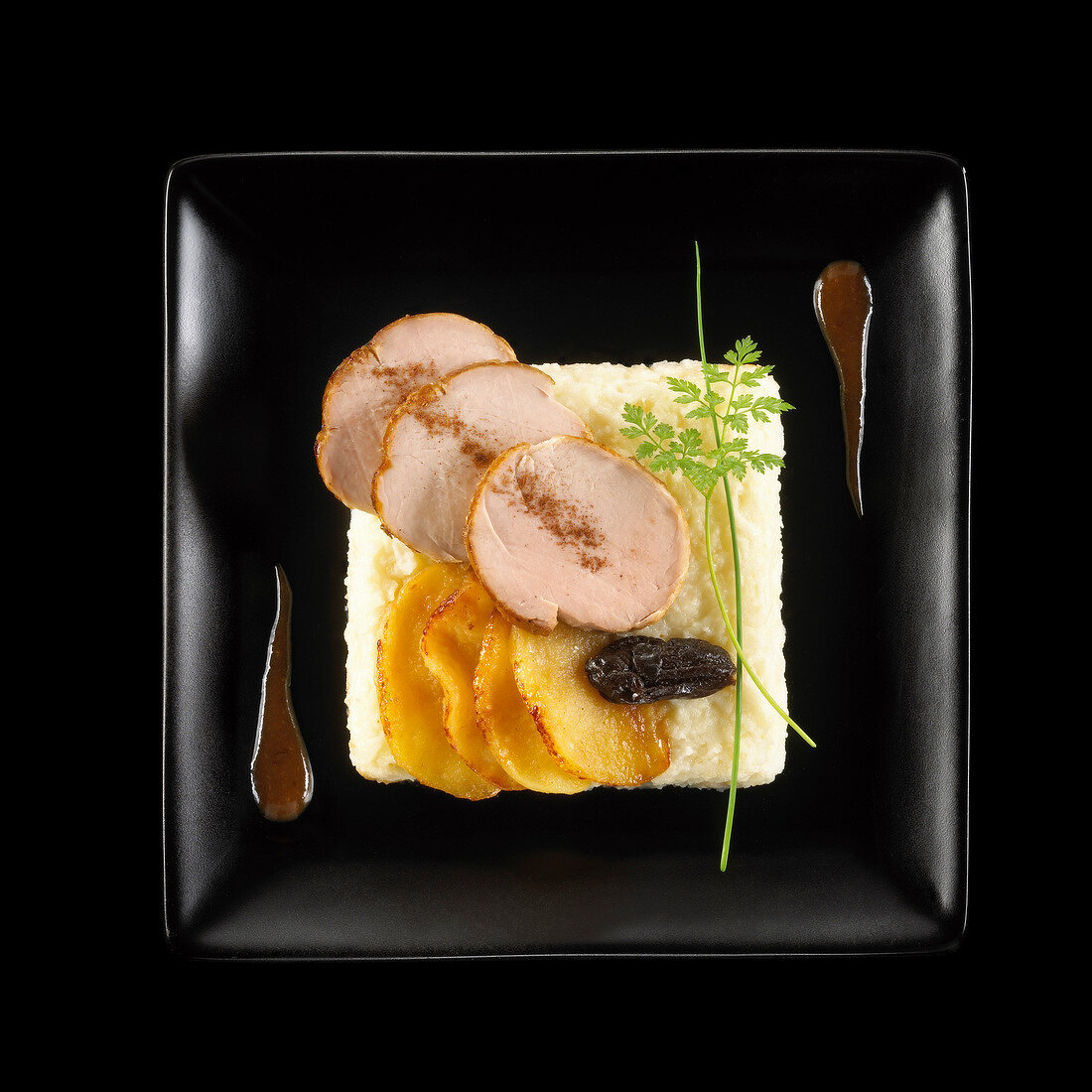 Pan-fried fillets of pork,celeriac mash,sauteed potatoes and prune on a black background