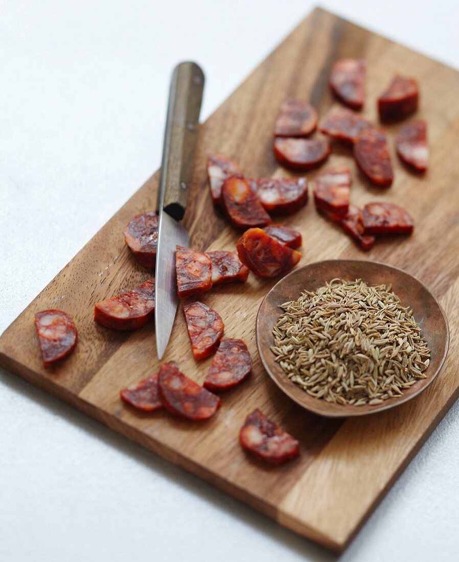 Geschnittene Chorizo auf Holzbrett und Schale mit Kreuzkümmelsamen