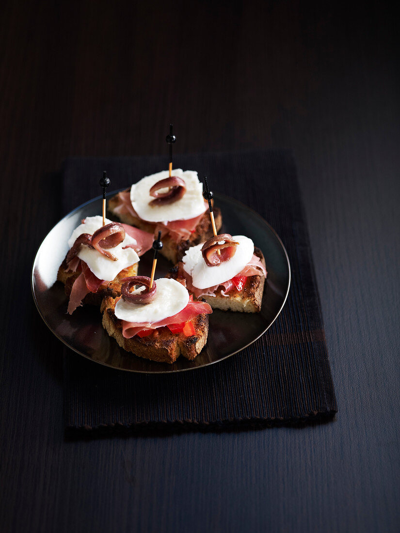 Brothäppchen mit Tomate, Schinken, Mozzarella und Sardellen