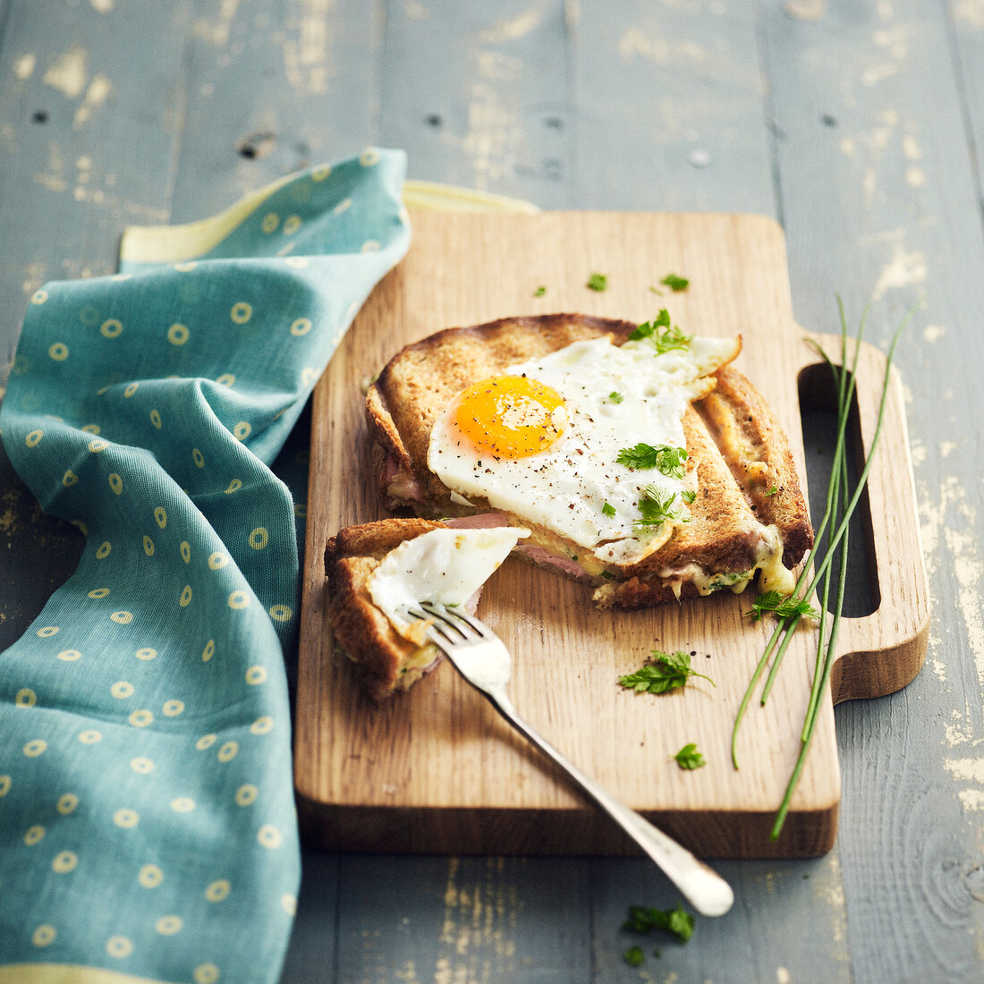 Cheese and ham toasted sandwich topped with a fried egg and sprinkled with herbs