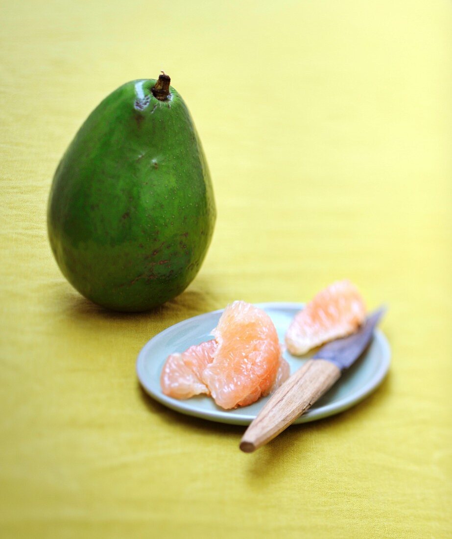 Grapefruitfilets auf kleinem Teller mit Messer, dahinter eine Avocado