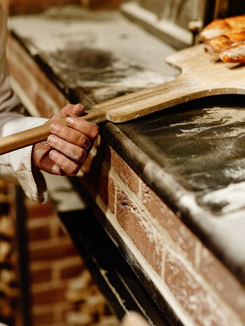 Bäcker holt frisch gebackene Baguettes aus dem Holzofen